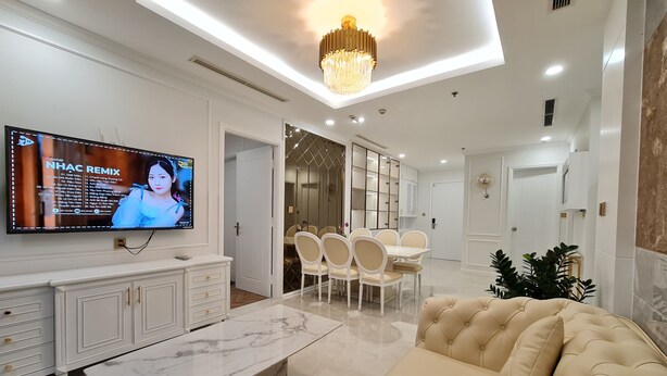 Una sala de estar moderna con televisor, una mesa de centro de mármol, un sofá color beige y un comedor con sillas y una mesa.