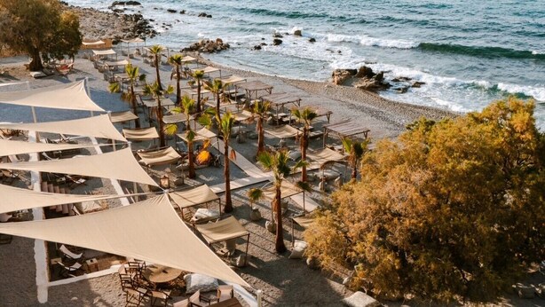 Ett semesterhotell vid stranden med solstolar, parasoller och en klippig kustlinje.