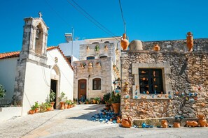 A traditional stone building with a window displaying pottery, a bell tower, and a paved street with potted plants. - Stylish Villa w/ Heated Pool & BBQ, near Rethymno (Rethymnon)