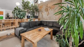 En moderne stue med en sort lædersofa, et træbord og flere potteplanter.