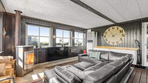 En moderne stue med en stor lædersofa, pejs og et ur på væggen.