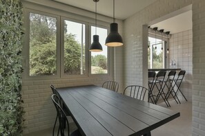 Ein Essbereich mit Holztisch und Stühlen, großen Fenstern und hängenden Pendelleuchten.