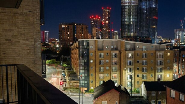Vista noturna da cidade com arranha-céus, uma rua e um edifício com várias janelas e varandas.