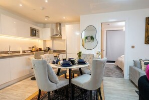 A modern kitchen with white cabinets, a stainless steel range hood, and a dining area with a round table and four chairs. - Skyline views, two king bedrooms and free parking near MediaCityUK (Greater Manchester)