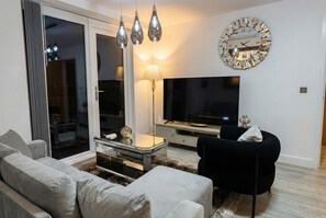 A modern living room with a sofa, a black armchair, a glass coffee table, a TV, and a decorative clock. - Skyline views, two king bedrooms and free parking near MediaCityUK (Greater Manchester)