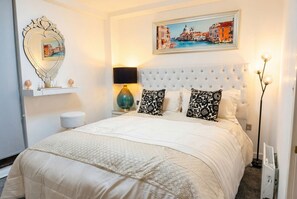 A bedroom with a tufted headboard, a bed with white bedding, a decorative mirror, a framed cityscape picture, and a bedside lamp. - Skyline views, two king bedrooms and free parking near MediaCityUK (Greater Manchester)