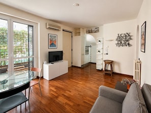 A modern living room with a glass dining table, a gray sofa, and a kitchen area in the background. - BIG Fiera Terrace (Amendola - Duomo M1) (Milan)