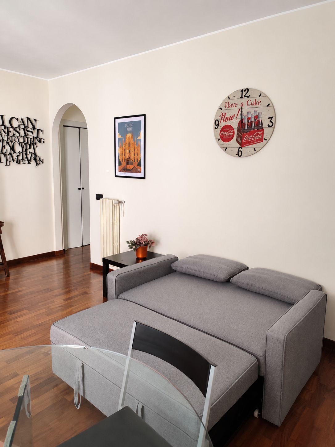 Ein modernes Wohnzimmer mit einem grauen Sofa, einem Glastisch und einer Wanduhr.