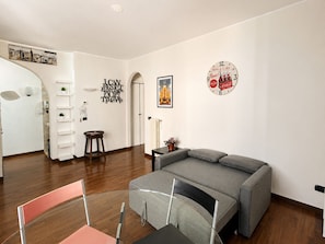 A modern living room with a grey sofa, a glass dining table, and a wall clock. - BIG Fiera Terrace (Amendola - Duomo M1) (Milan)