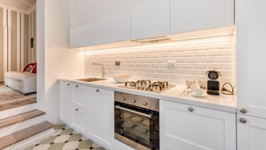 Een moderne keuken met witte kasten, een inbouwoven en een aanrecht met een koffiezetapparaat en kopjes.