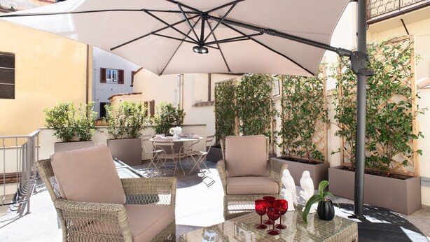 Een terras buiten met rieten meubels, een glazen tafel en een grote parasol.