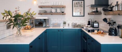 Una cocina con armarios azules, encimeras blancas, lámparas colgantes y una cita enmarcada en la pared.