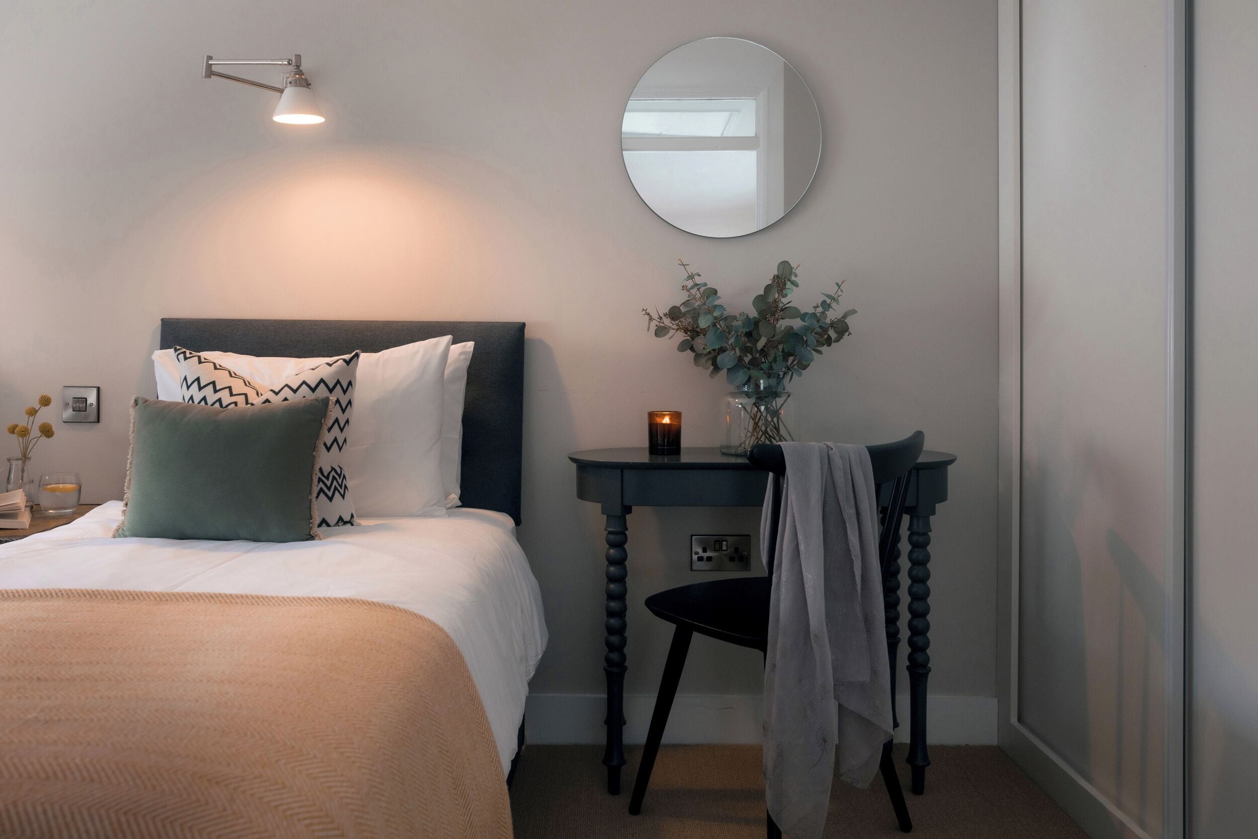 Une chambre à coucher comprenant un lit, une table de chevet, un miroir et une lampe fixée au mur.