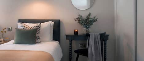 A bedroom with a bed, bedside table, mirror, and a wall-mounted lamp.