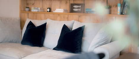 A light-colored sofa with dark cushions, a wooden shelf with books and decorative items, and a blurred foreground.