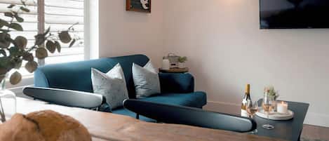 A living room with a blue sofa, a coffee table with a candle, and a television mounted on the wall.