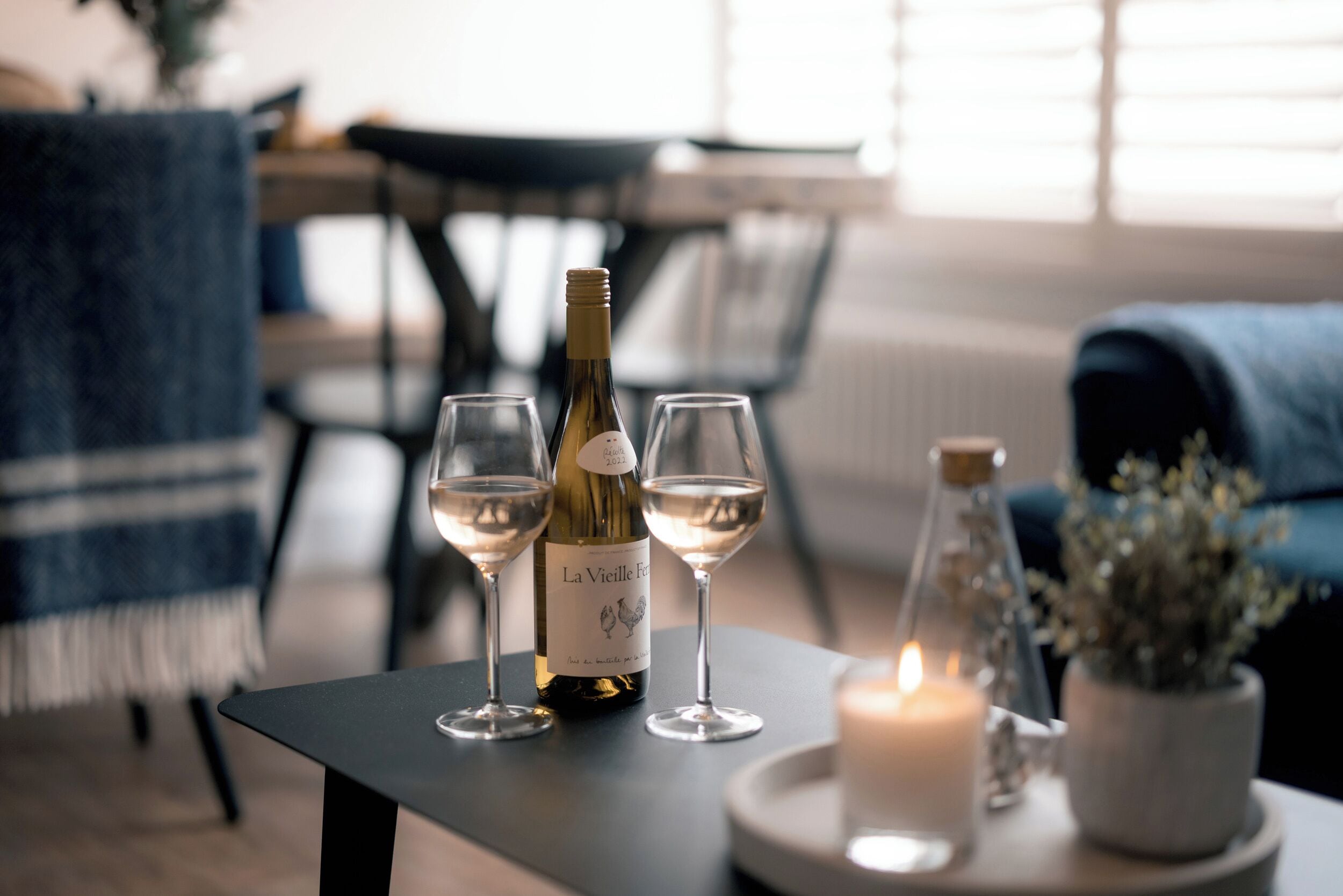En vinflaska och två glas på ett bord, tillsammans med ett ljus och en krukväxt.