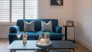 Een woonkamer met een blauwe bank, een bijzettafeltje met een kaars, een fles en een glas witte wijn.