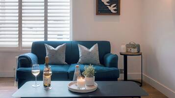 Ein Wohnzimmer mit einem blauen Sofa, einem kleinen Tisch mit Kerze, einer Flasche und einem Glas Weißwein.