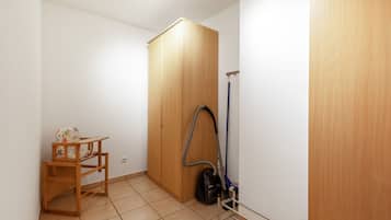 A small room with a wooden wardrobe, a vacuum cleaner, and a small wooden table with a chair.