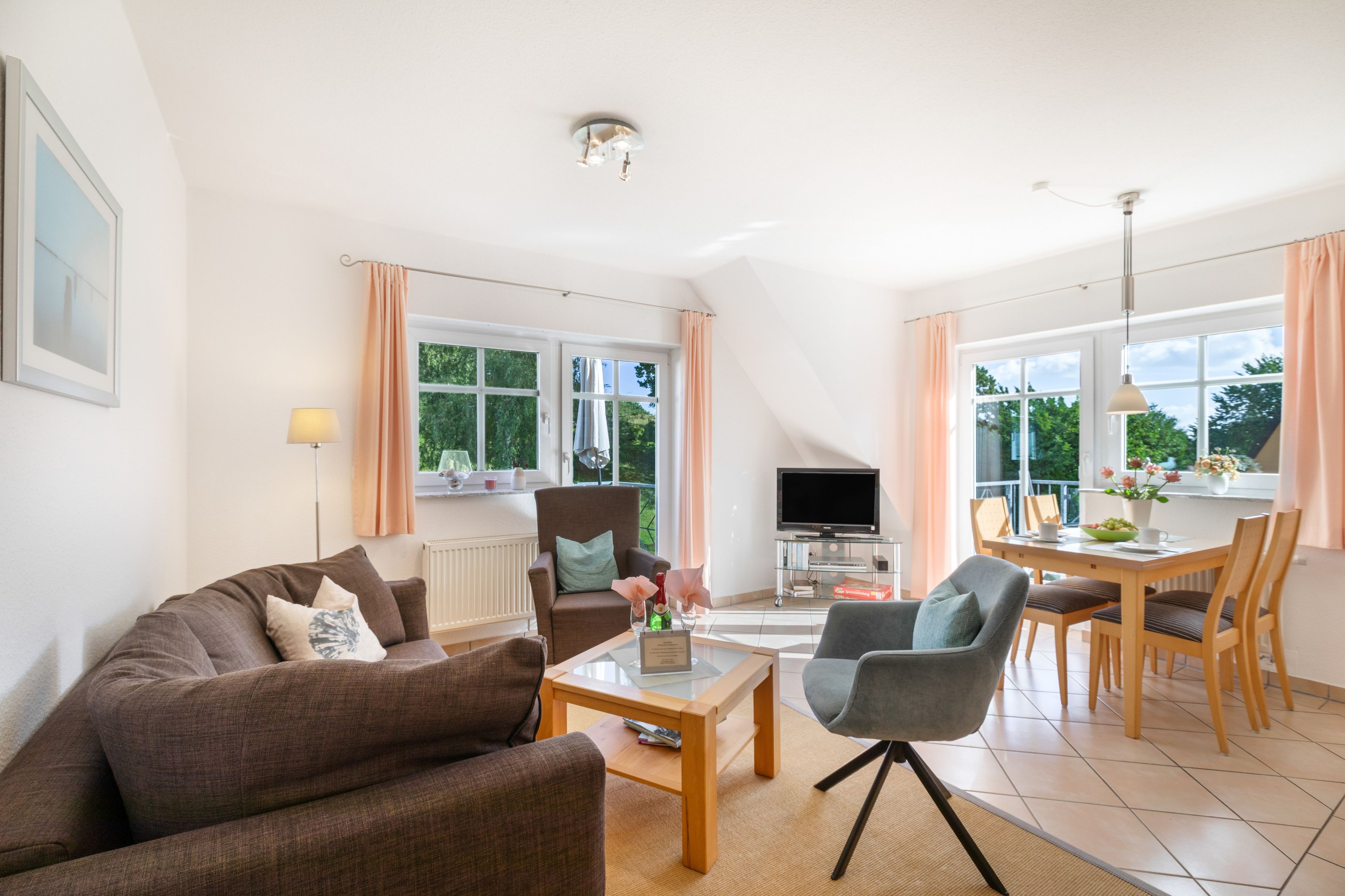 Ein modernes Wohnzimmer mit einer Couch, Sesseln, einem Couchtisch, einem Fernseher und einem Essbereich mit Stühlen und einem Tisch.