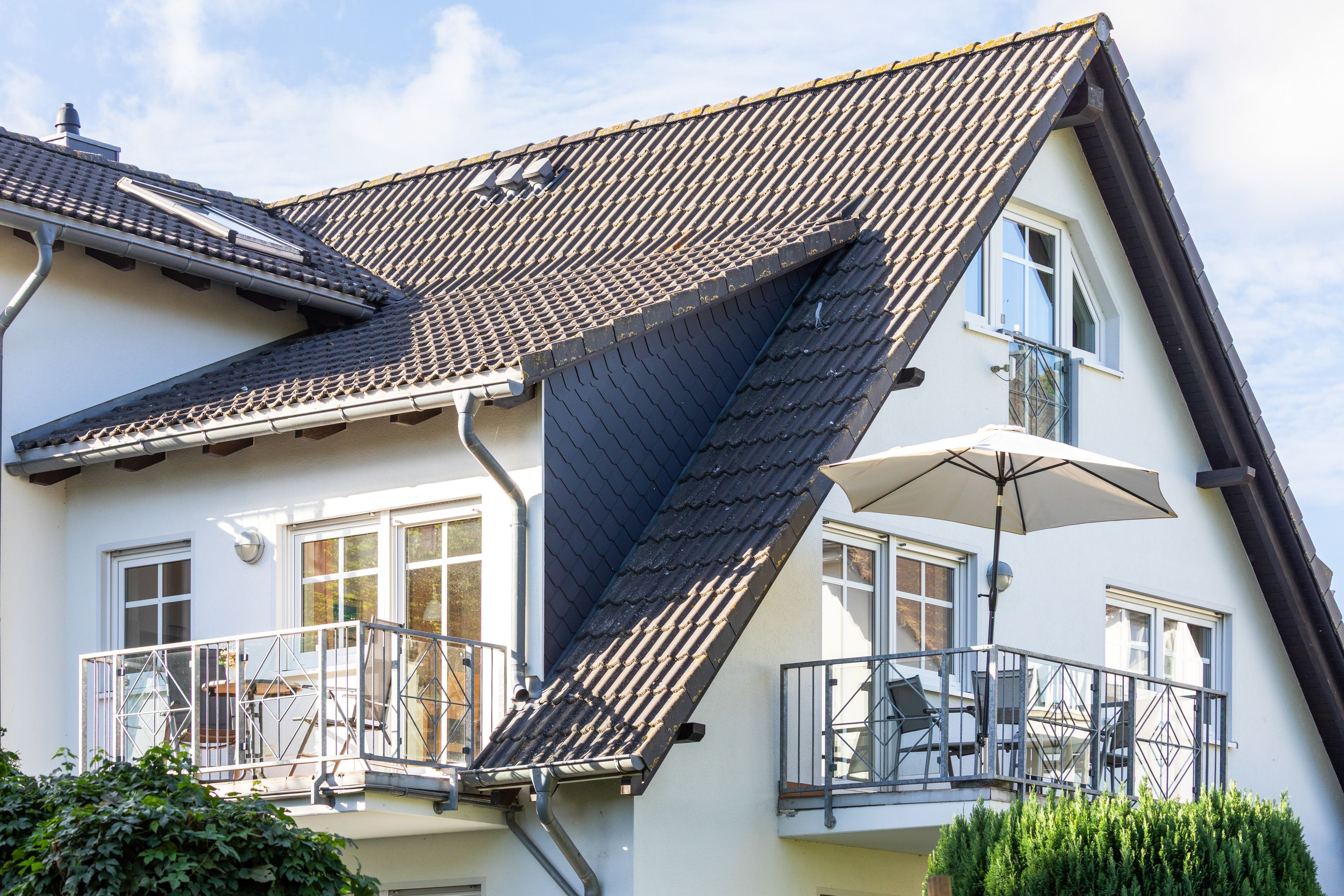 Ein zweistöckiges Gebäude mit geneigtem Dach, großen Fenstern und einem Balkon mit Geländer.
