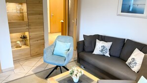 Un salon moderne avec un canapé gris, un fauteuil bleu et une table basse sur laquelle est posé un vase de fleurs.