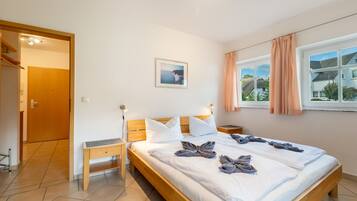A hotel room with a wooden bed, a bedside table, a nightstand, a window with curtains, and a framed picture on the wall.