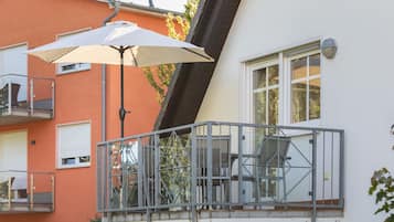 Ein Balkon mit Metallgeländer, einem weißen Sonnenschirm und einem Stuhl.