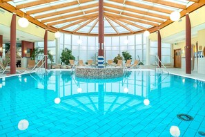 An indoor swimming pool with a tiled floor, wooden beams, and a central mosaic feature. - Dune House with Pool Access in Prime Location (Göhren)