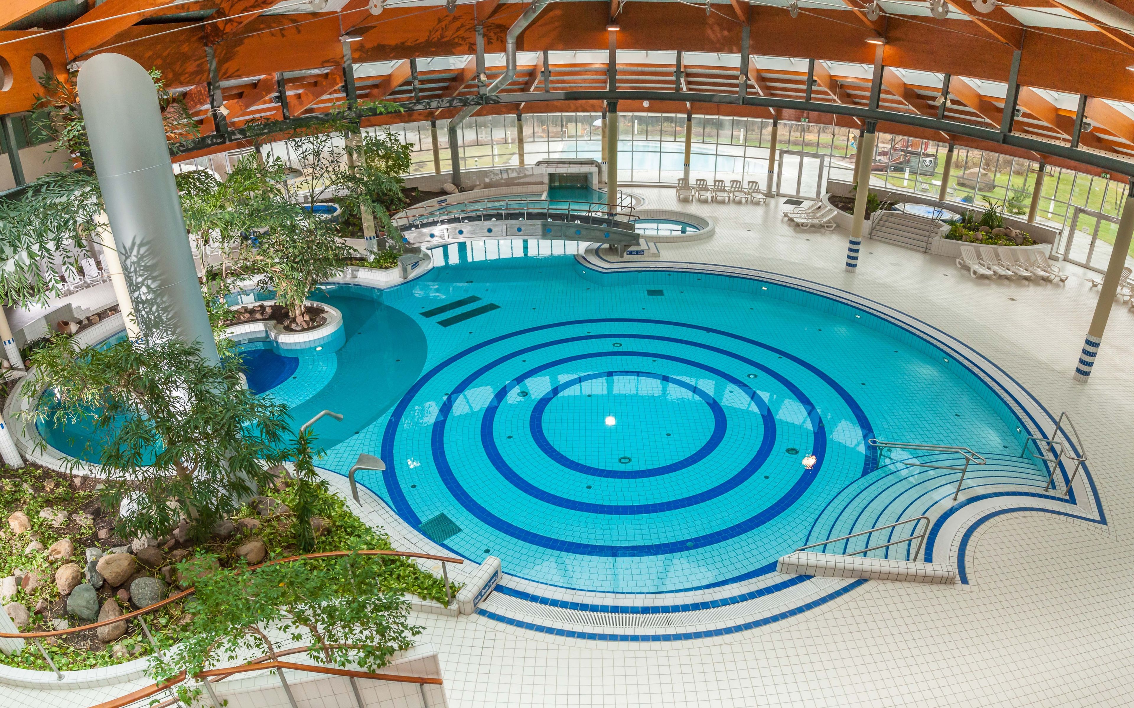 En indendørs swimmingpool med flere baner, et springbræt og et opholdsområde med stole.