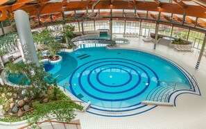 Ein Hallenbad mit mehreren Bahnen, einem Sprungbrett und einer Sitzgelegenheit mit Stühlen.