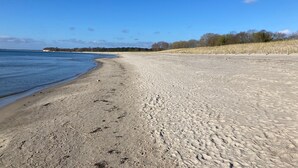 A wide sandy beach with gentle waves, a clear sky, and sparse vegetation. - Apartment 'Fewo Südstrand Schwimmbadnutzung' with Sea View, Sauna and Wi-Fi (Göhren)