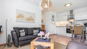 A modern living room with a sofa, a coffee table, and a dining area with chairs and a kitchen in the background. - Apartment 'Fewo Südstrand Schwimmbadnutzung' with Sea View, Sauna and Wi-Fi (Göhren)