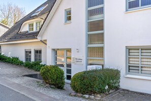 Ein Gebäude mit einem Schild, auf dem 'Ferienhaus Sudstrand' steht, einem befestigten Eingangsbereich und einer kleinen Hecke.