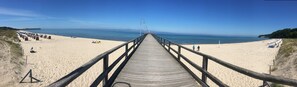 Ein Holzsteg führt zu einem Sandstrand mit freiem Blick auf den Ozean.