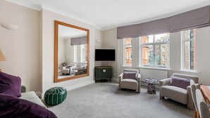 Een moderne woonkamer met een grote spiegel, een flatscreen televisie en uitzicht op gebouwen door grote ramen.