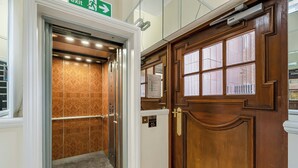 Een lift met een behangetje, een houten deur met glaspanelen en een nooduitgangsbord.