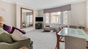 Een moderne woonkamer met een bank, fauteuil, eettafel en een grote spiegel.