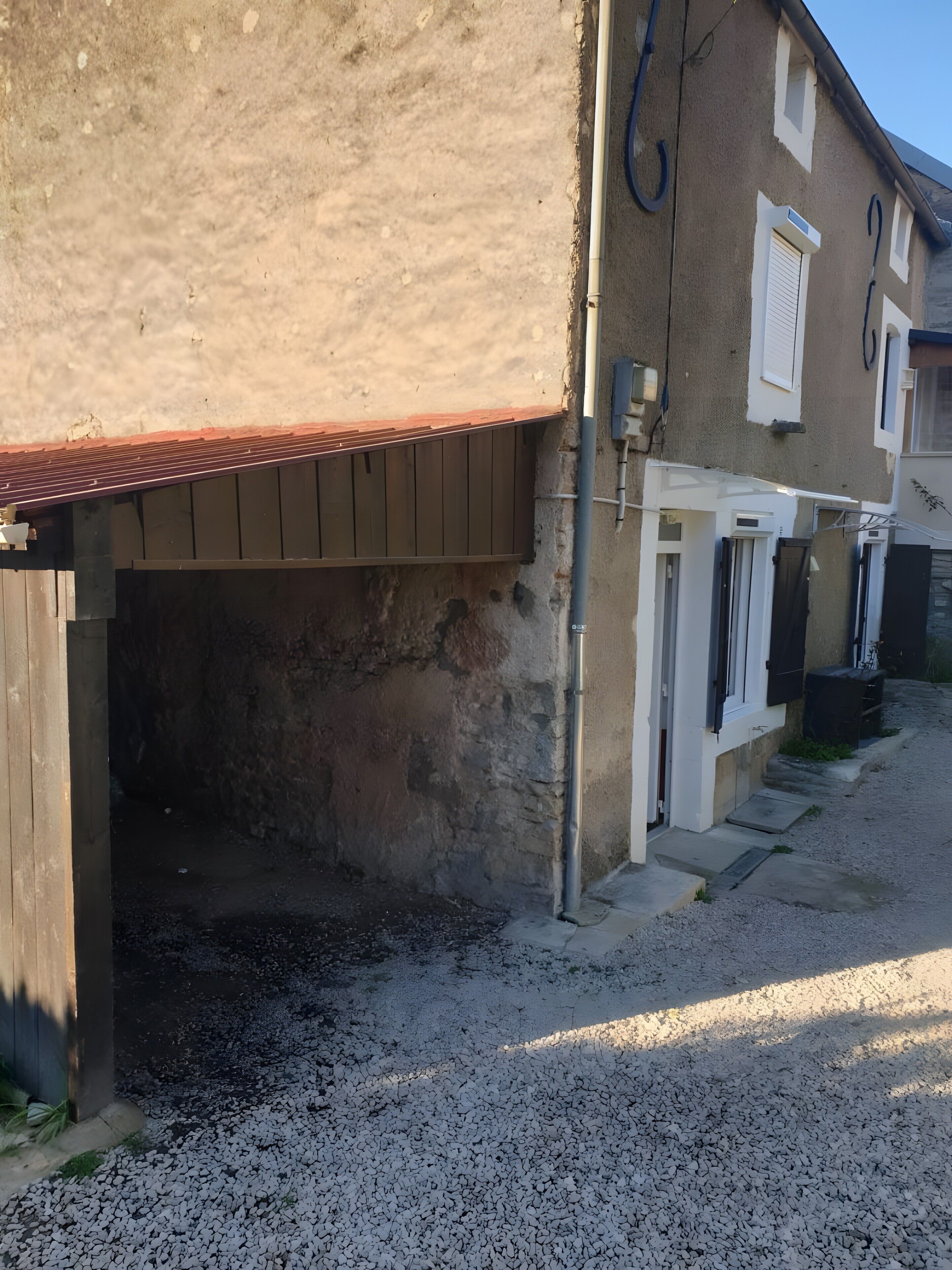 Un immeuble résidentiel avec une allée en gravier, une clôture en bois et un toit en métal.