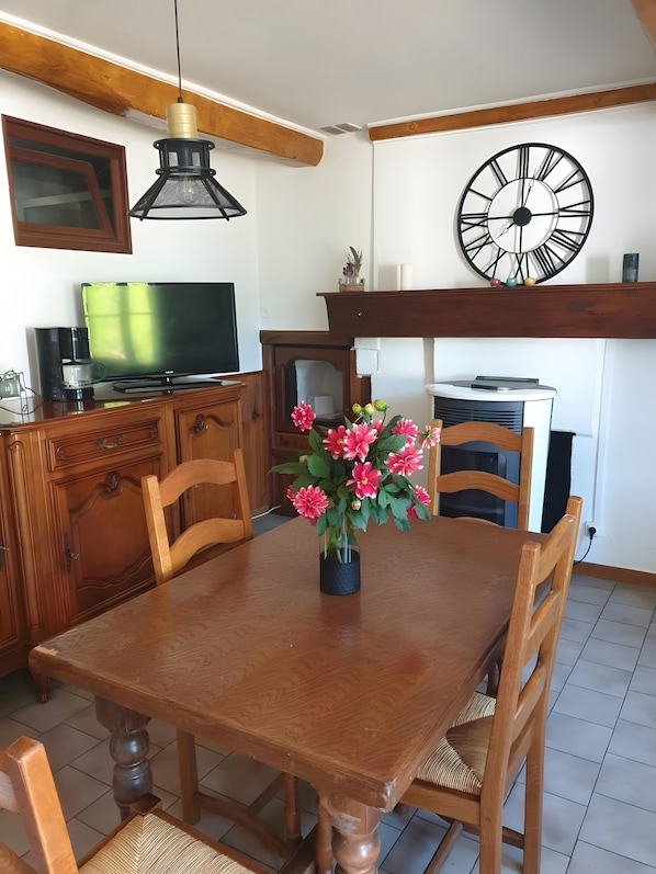 A dining area with a wooden table, chairs, a vase of flowers, a clock, and a television on a cabinet.