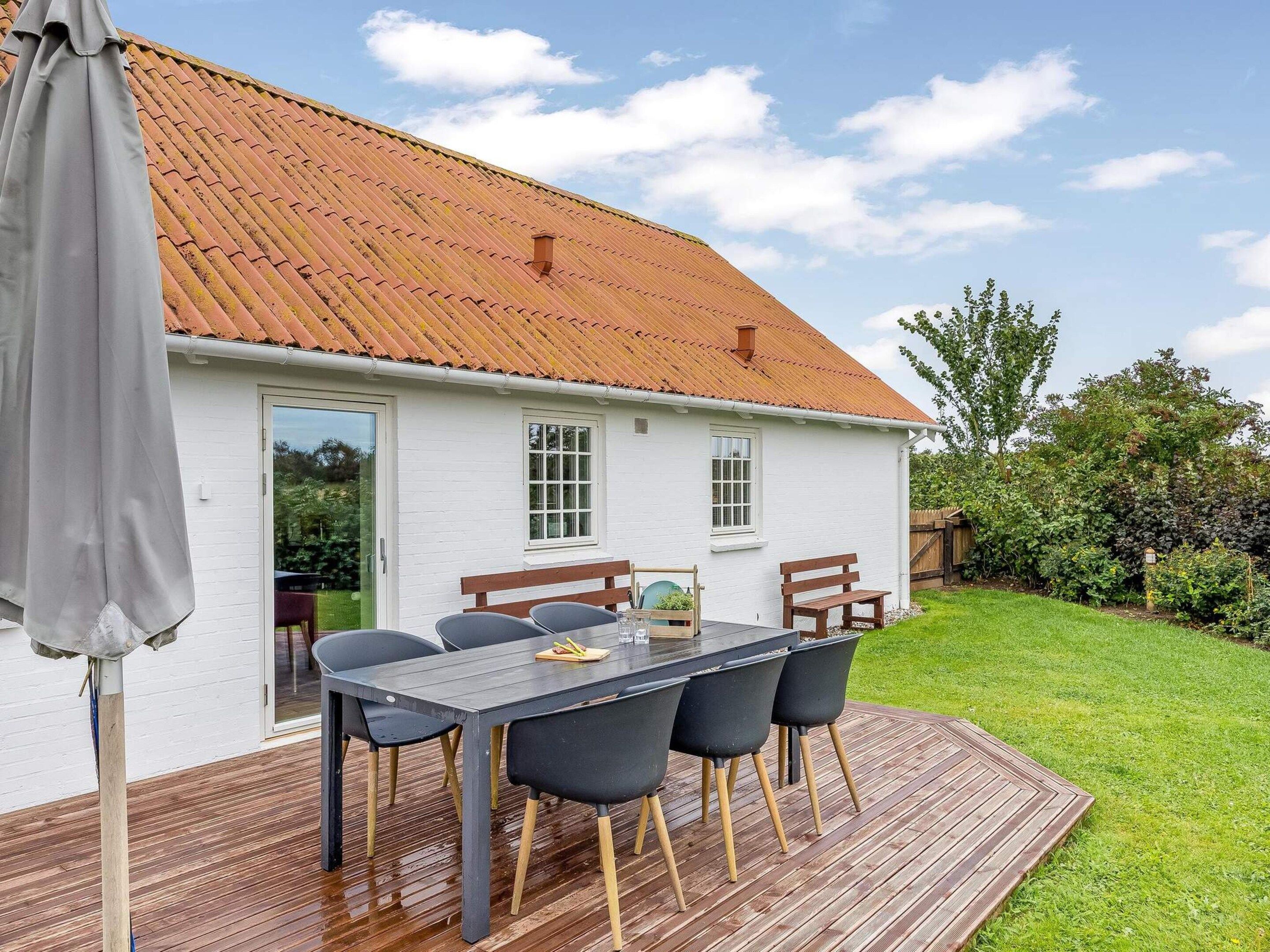 Una casa blanca con techo de tejas, una terraza con mesa y sillas, y un jardín.