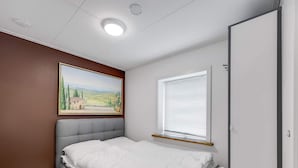 Ein Schlafzimmer mit Bett, Nachttisch, einem Gemälde, einem Fenster mit Jalousien und einer Tür.