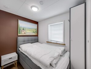 Ein Schlafzimmer mit Bett, Nachttisch, einem Gemälde, einem Fenster mit Jalousien und einer Tür.
