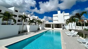 Una piscina con edificios blancos, palmeras y un cielo azul despejado.