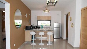 Una cocina moderna con una isla central, taburetes de bar, un refrigerador y un ventanal grande.