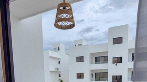 Un balcón con mobiliario de mimbre, un colgador de luces y vistas a un complejo de edificios blancos.