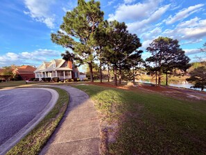 A residential area with a house, a curved driveway, a pond, and surrounding trees.