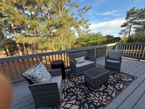 Une terrasse dotée de meubles en osier, d’un tapis à motifs et offrant une vue sur les arbres.