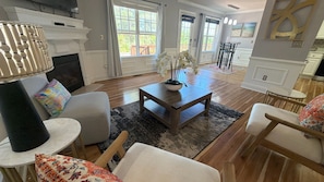 A living room with a fireplace, a coffee table with orchids, and a dining area with chairs and a table.